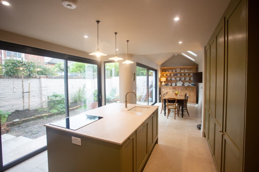Open-plan kitchen-dining space featuring full-height sliding doors and green cabinetry.
