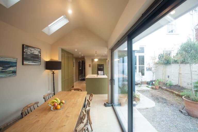 Dining area with vaulted ceiling, skylights, and garden-facing glazing leading back to the kitchen island.