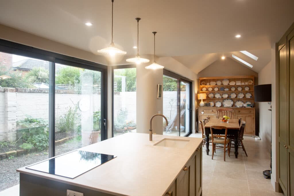 View from dining area toward kitchen showing island, full glazing, and fitted cabinets.