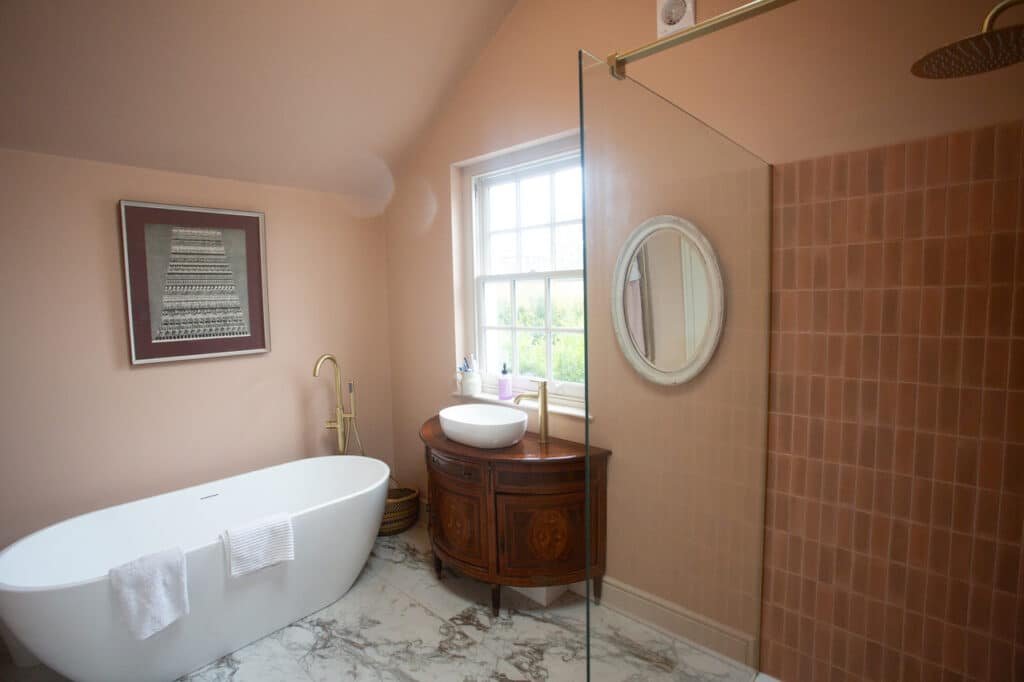 Elegant bathroom with freestanding bath, marble-effect flooring, pink tiled shower wall, and antique vanity unit.